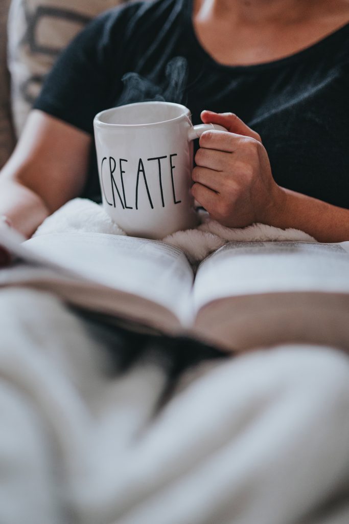 Photo of person reading a book with a coffee cup in their hand that says CREATE.
 
Photo by Nathan Dumlao on Unsplash